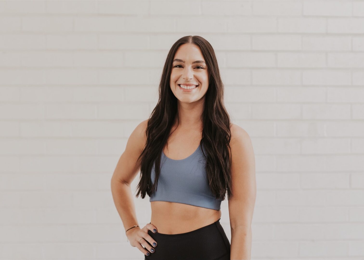 Smiling woman in workout attire against wall.
