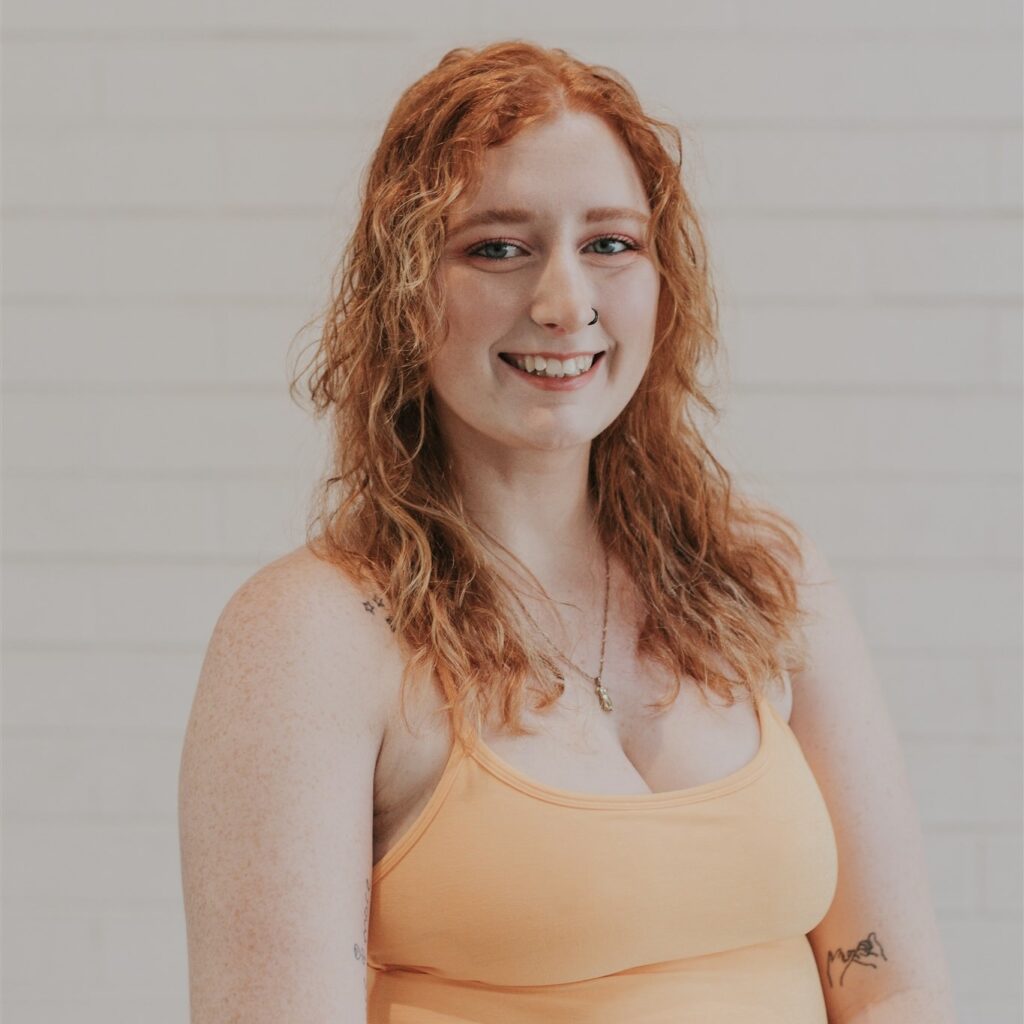 A woman with red hair and a peach colored top.