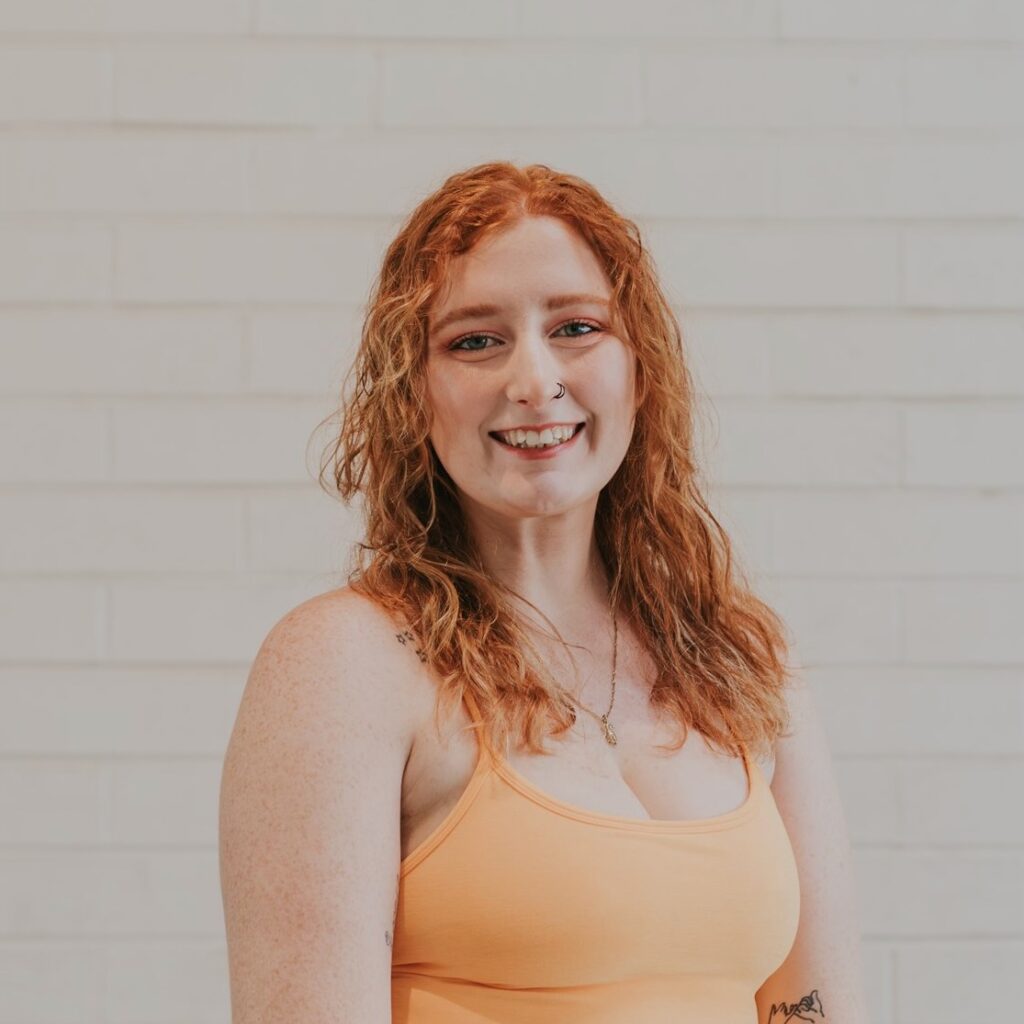 A woman with red hair standing in front of a white wall.