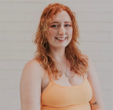 A woman with red hair and a peach colored top.