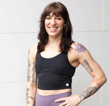 Woman with tattoos smiling in workout attire.