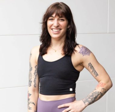 Woman with tattoos smiling in workout attire.