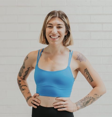 A woman with tattoos standing in front of a white wall.