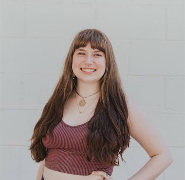 Smiling woman posing against white wall.