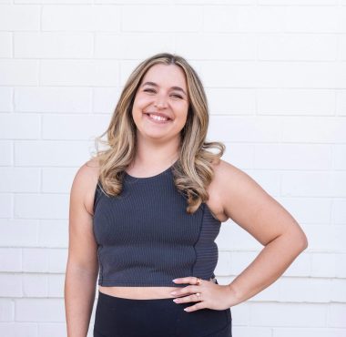 Smiling woman standing against white brick wall.