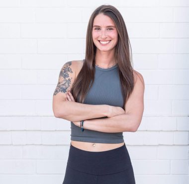 Woman smiling with arms crossed, white background.
