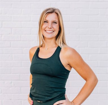 Smiling woman in activewear against white brick.
