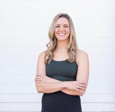Smiling woman standing against white brick wall.