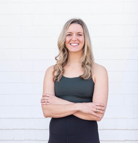 Smiling woman standing against white brick wall.