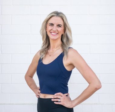 Smiling woman in athletic attire against wall.