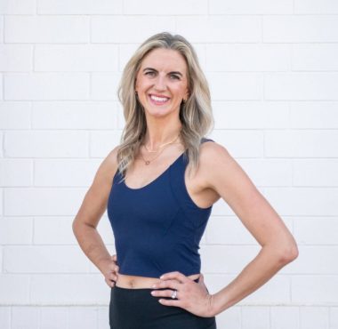 Smiling woman in athletic attire against wall.