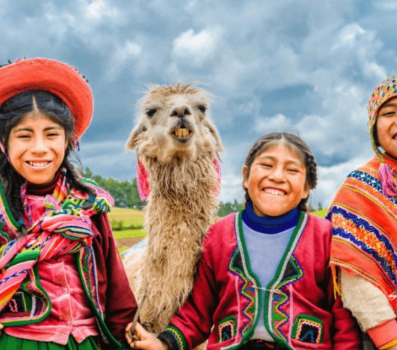 Smiling girls and llama in colorful attire.