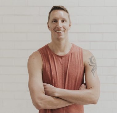 Man in red sleeveless shirt smiling confidently.