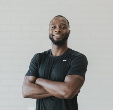 Smiling man in black shirt, arms crossed.