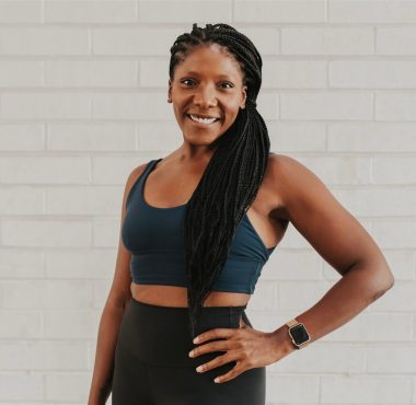 Smiling woman in activewear against brick wall.