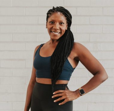 Smiling woman in activewear against brick wall.