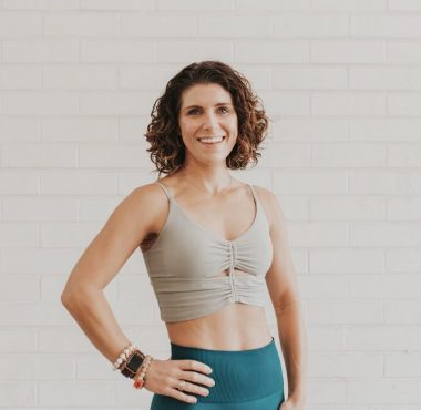 Woman smiling in athletic wear against wall.
