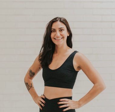 Smiling woman in athletic wear, brick background.