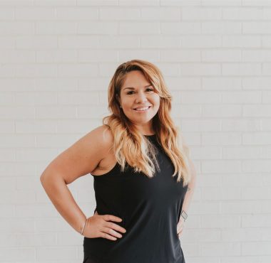 Woman smiling in front of white brick wall.