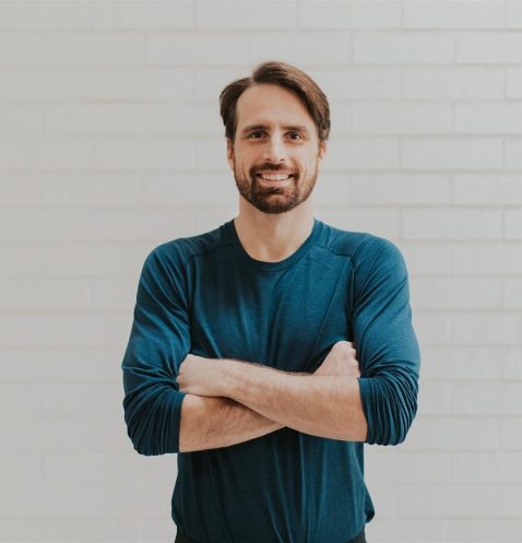 Man smiling with arms crossed, white background.