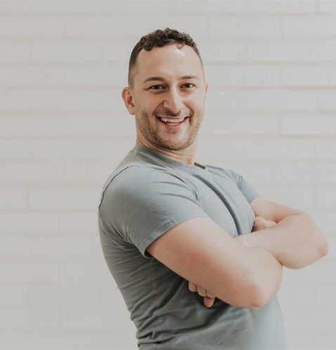 Smiling man with arms crossed, white background.
