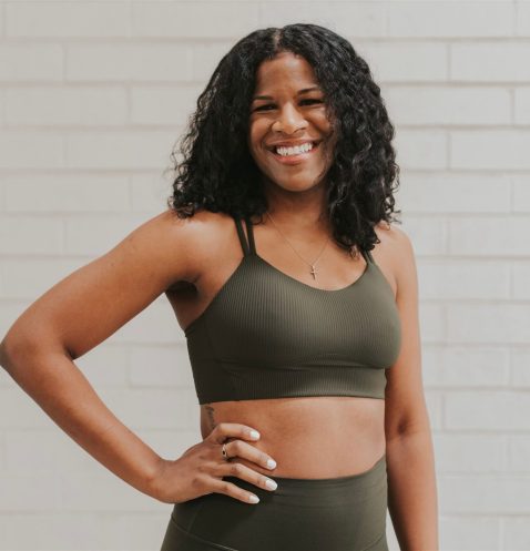 Woman smiling in athletic wear against brick wall.
