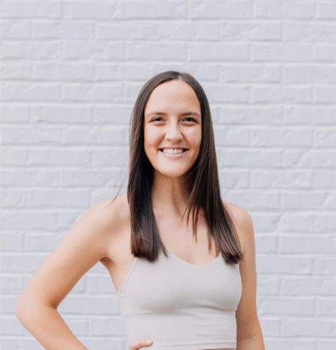 Smiling woman in workout attire, brick background.