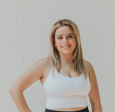 Smiling woman in workout attire against wall.