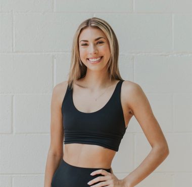 A woman in black sports bra standing next to a white wall.