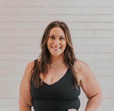 Smiling woman in black outfit, brick background.