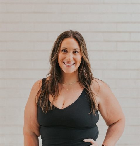 Smiling woman in black outfit, brick background.