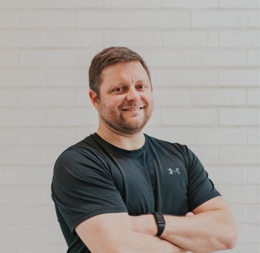 Man in black shirt smiling confidently.