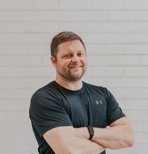 Man in black shirt smiling confidently.