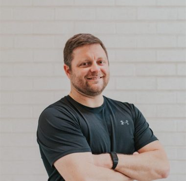 Man in black shirt smiling confidently.