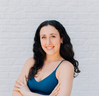 Woman smiling against a white brick wall.