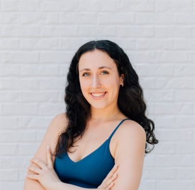 Woman smiling against a white brick wall.