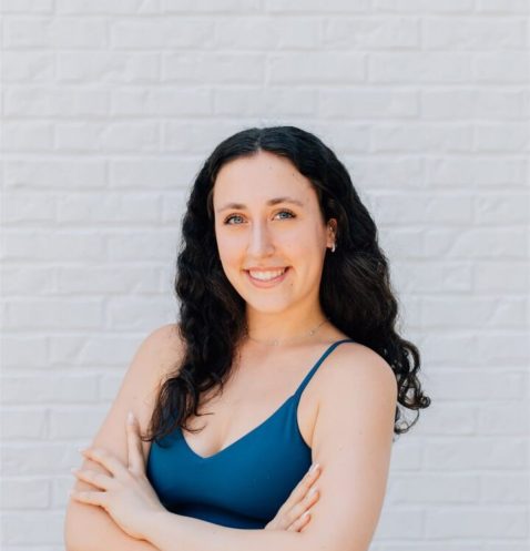 Woman smiling against a white brick wall.