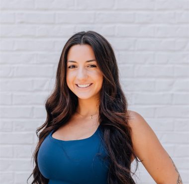 Smiling woman in athletic wear against brick wall.