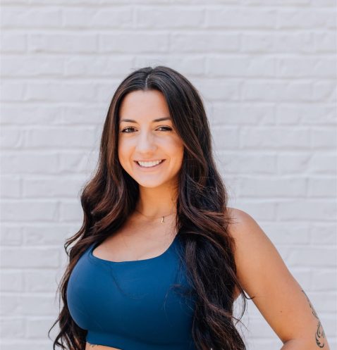 Smiling woman in athletic wear against brick wall.