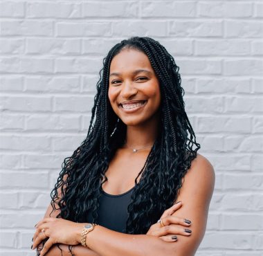 Smiling woman in black top, braided hair.