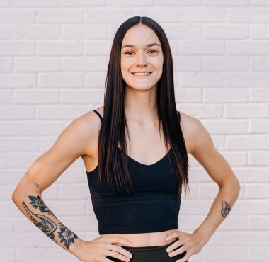 Smiling person with tattoos against brick wall.