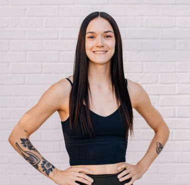 Smiling person with tattoos against brick wall.