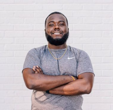 Man smiling with arms crossed against wall.